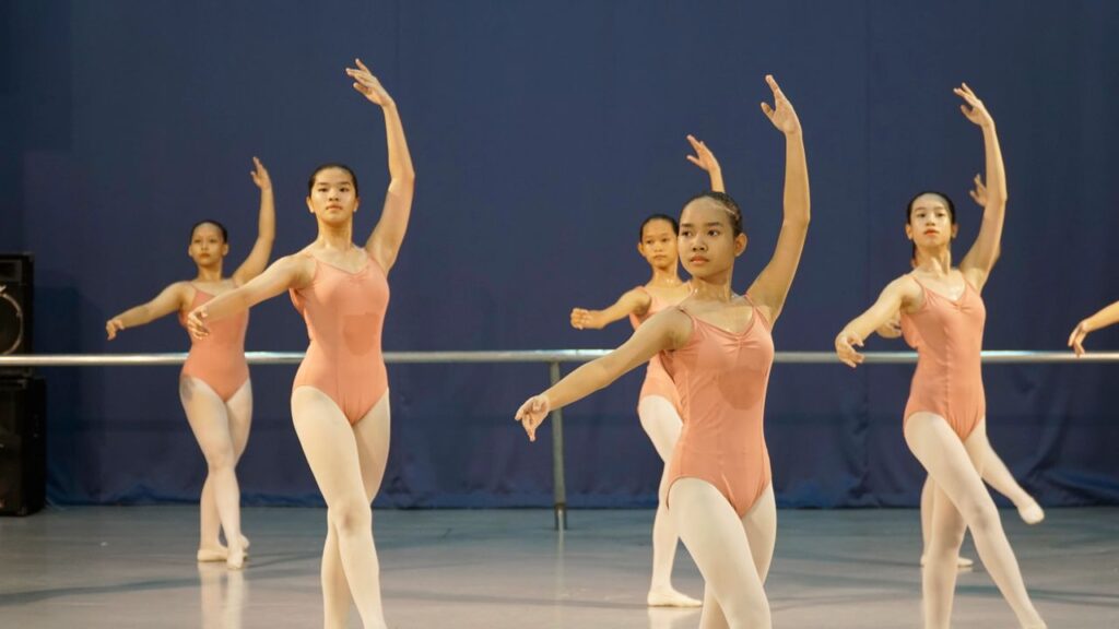 A group of young ballet dancers in pink leotards practicing in a dance studio.