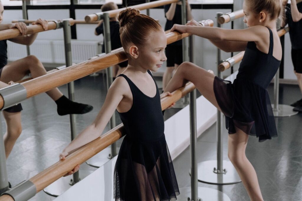 Young ballerinas in a studio practicing ballet techniques at the barre.