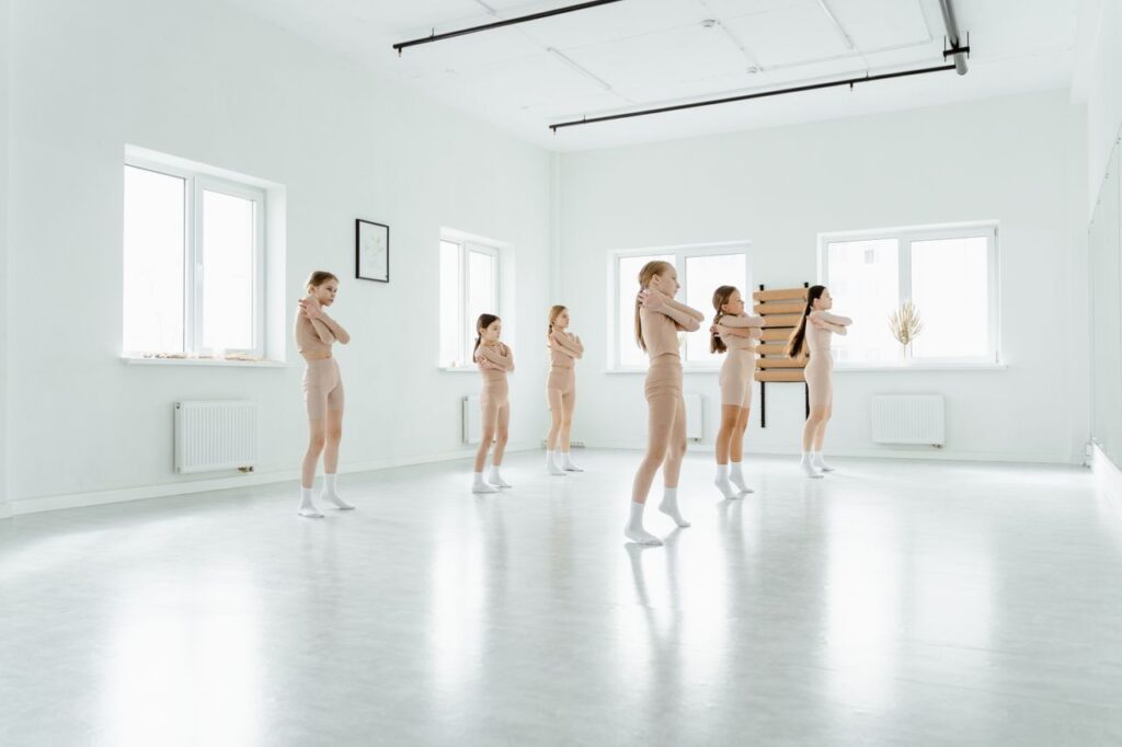 A group of young dancers practicing ballet moves in a minimalist, sunlit studio.